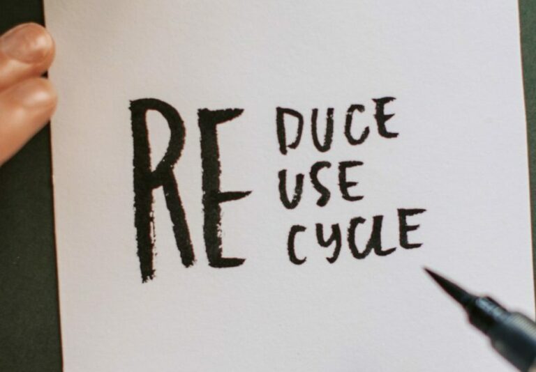 person writing reduce, reuse, recycle on a piece of paper