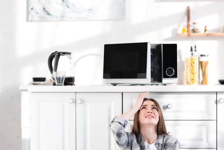 sad woman looking at broken microwave in kitchen