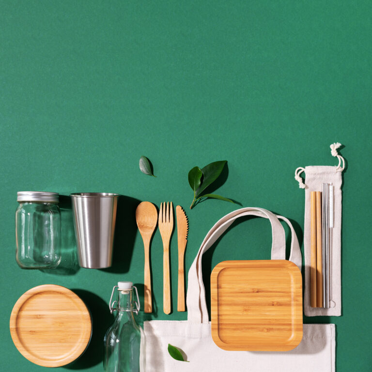 Sustainable lifestyle. Zero waste, plastic free shopping concept. Cotton bags, glass jar, bottle, metal cup, straws for drinking, bamboo cutlery and boxes on green background