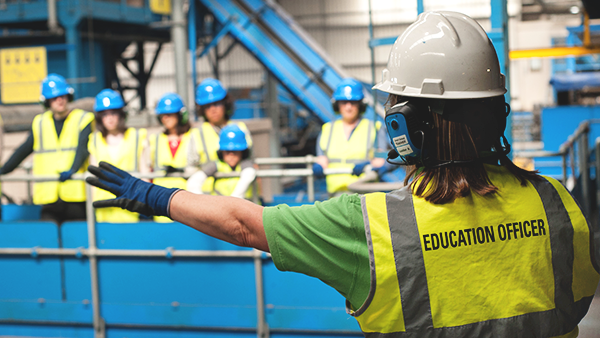 photo of an education officer in high-vis and hard-hat giving a tour of the Materials recovery facility to a group of visitors
