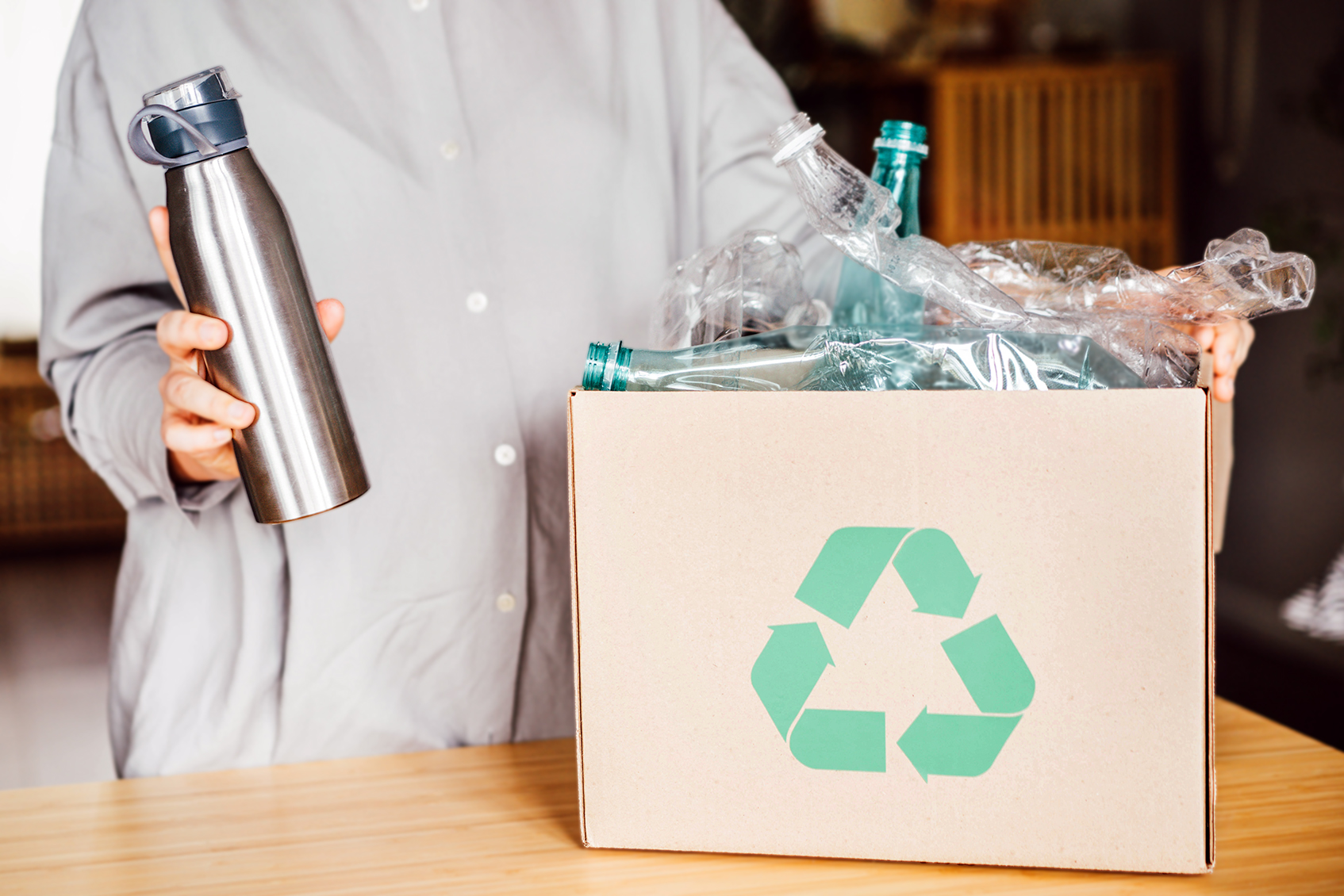 Person holding a reusable metal bottle in one hand, and a box of plastic bottles in the other hand.