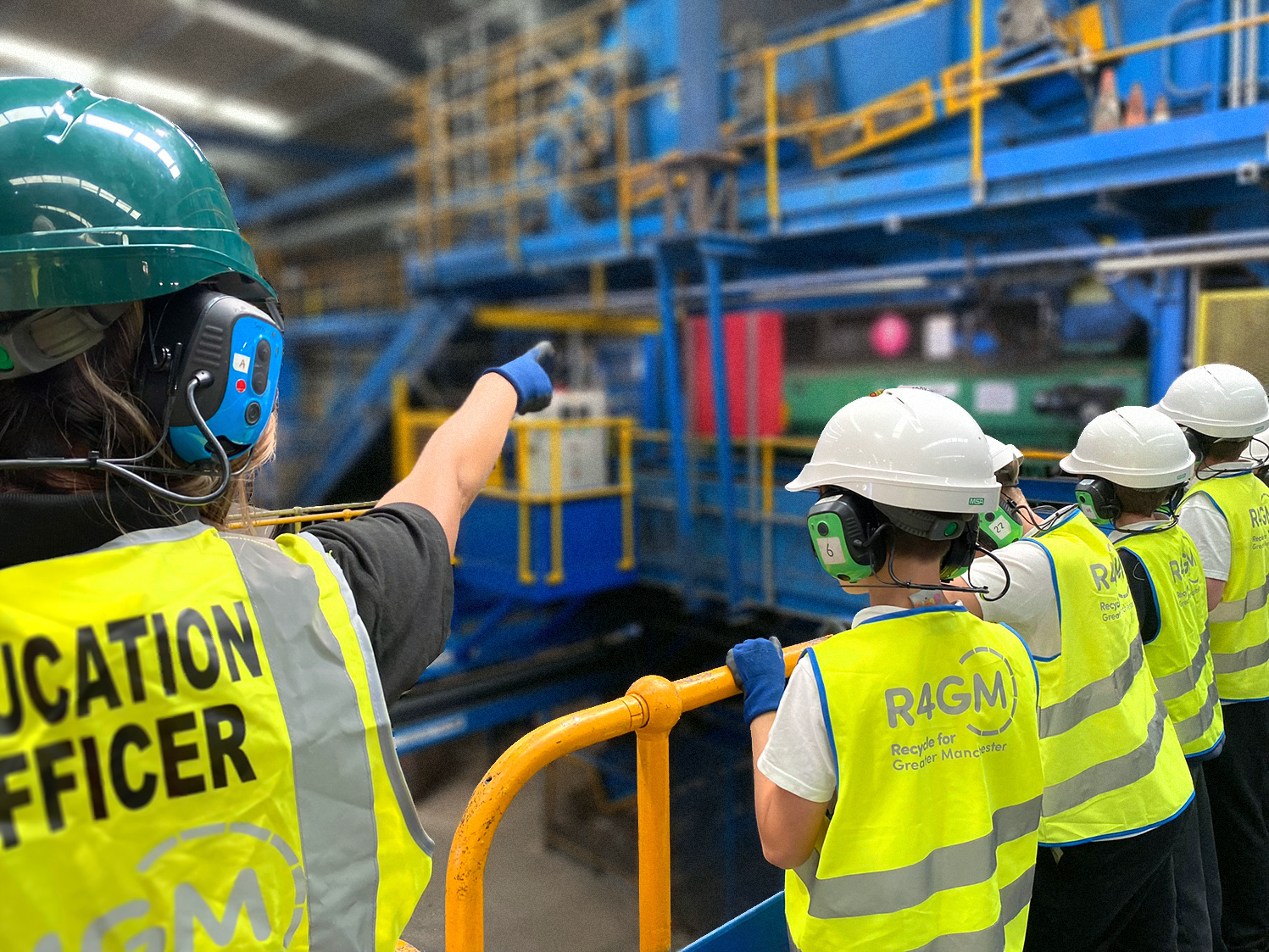 Education Officer pointing to a machine at a Materials Recovery Facility to a group of young visitors.