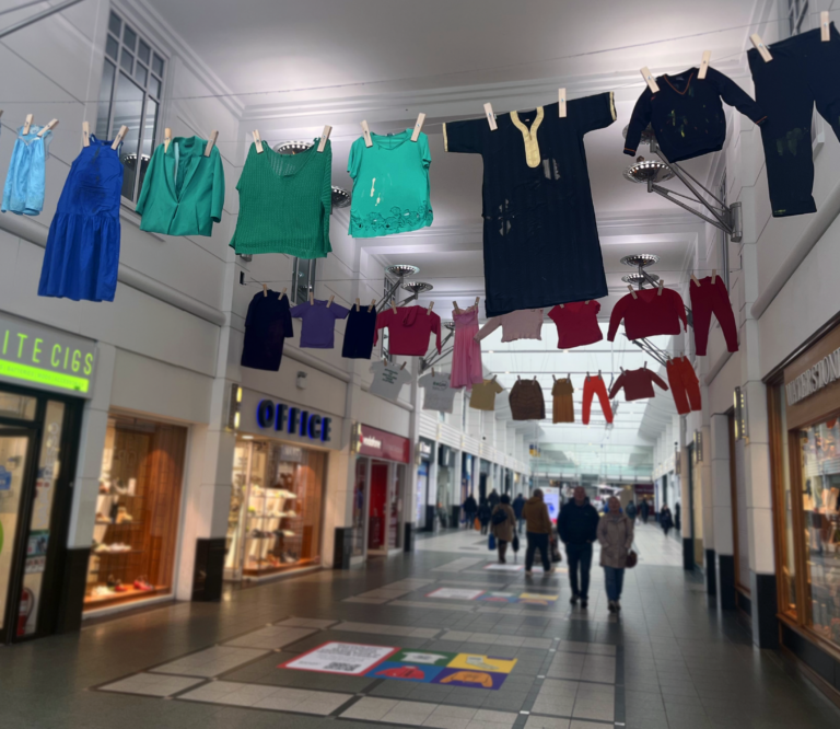 large washing line full of damaged clothing hanging over the walkway in a shopping centre.