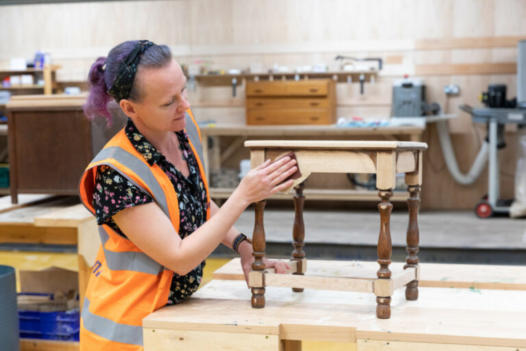 Woman renewing a piece of wooden furniture by sanding it down