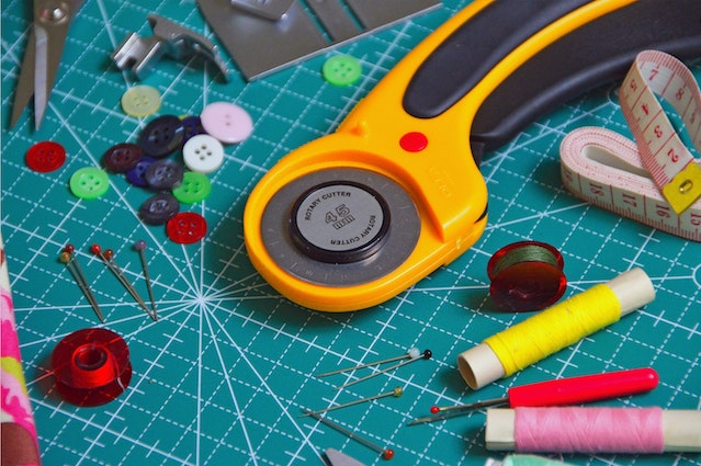 crafting items on a crafting mat, buttons, cotton thread, a cutter, measuring tape, scissors